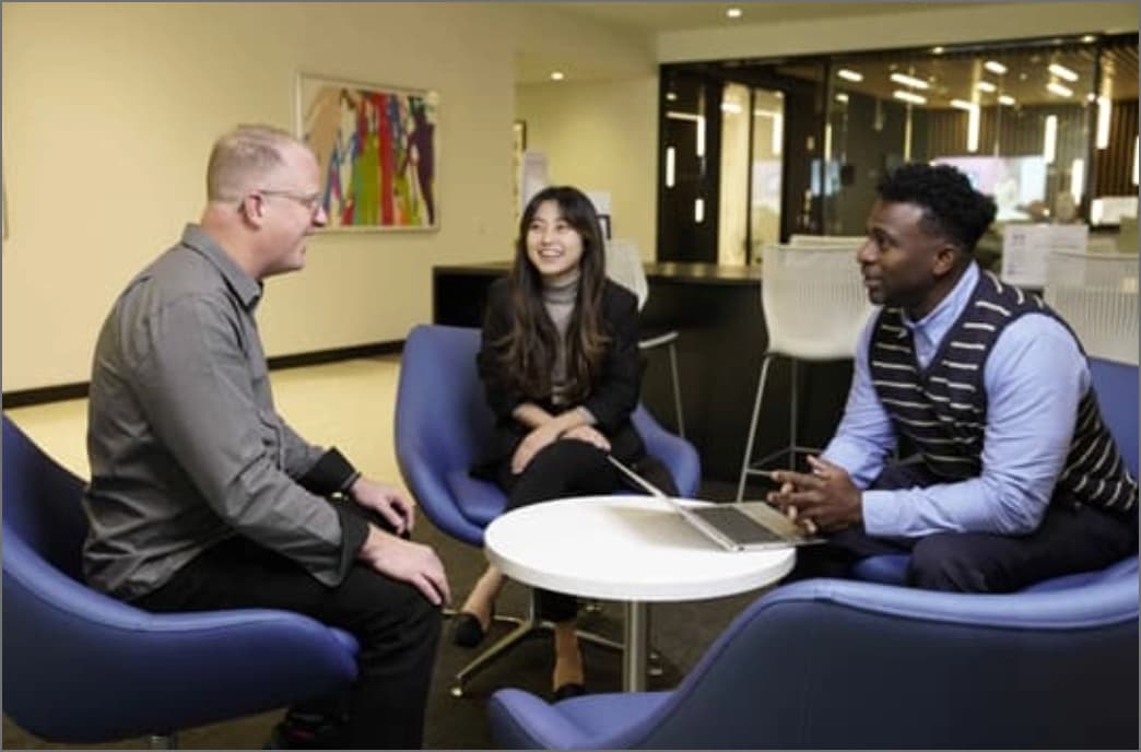 Three employees sitting in the common area of the office having a discussion