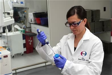 A scientist wearing protective equipment, using a pippette and sample tube to conduct research