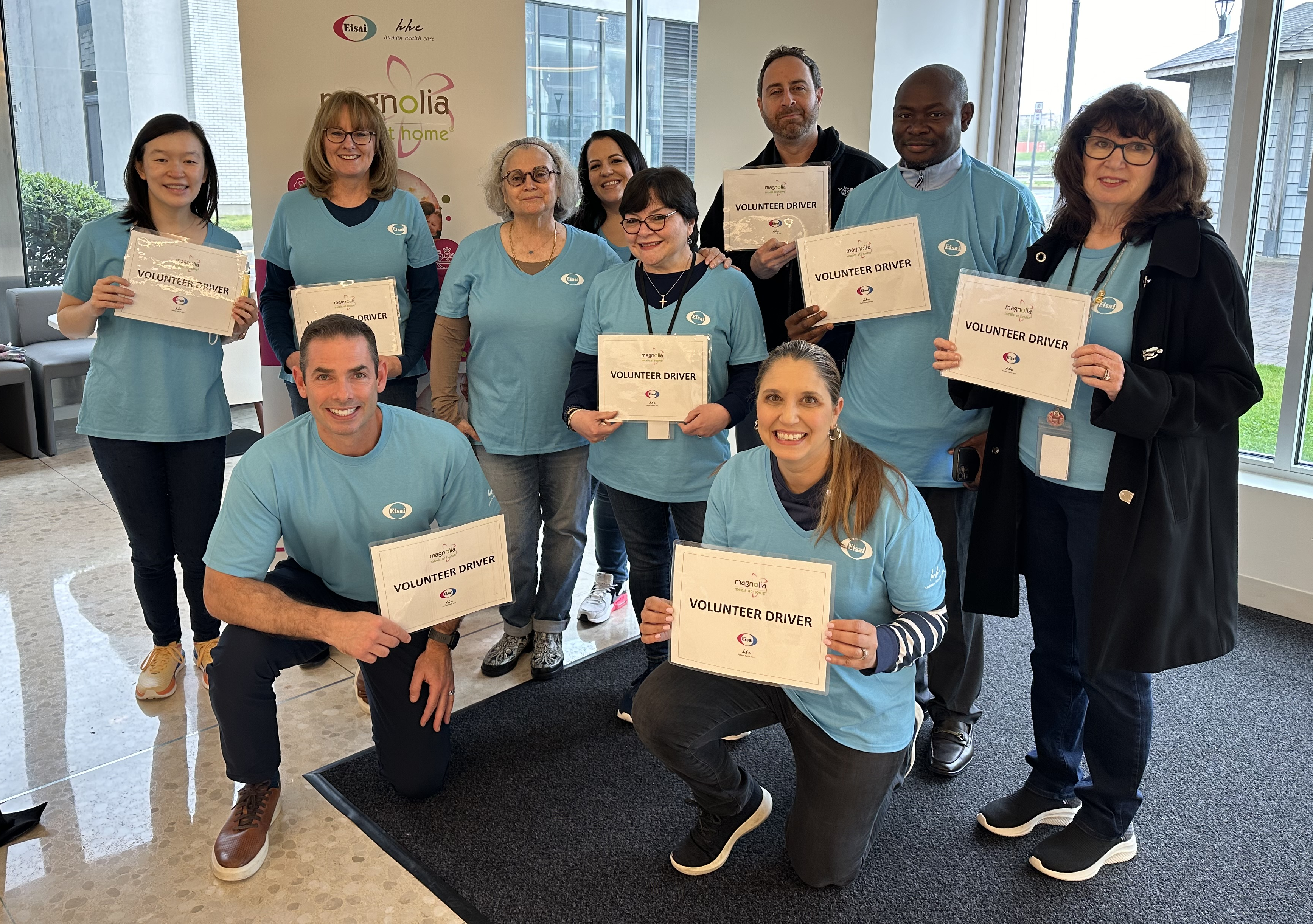 A group of Eisai employees in matching t-shirts featuring the Eisai logo that are holding signs that say volunteer driver