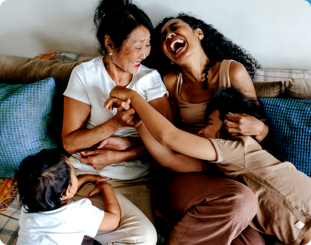 Two women playing with two children on a couch, and laughing