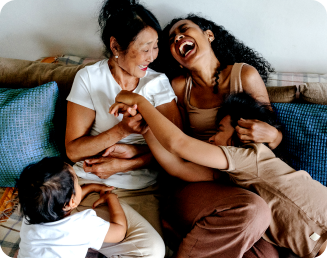 Two women playing with two children on a couch, and laughing