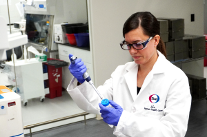 A scientist wearing protective equipment, using a pippette and sample tube to conduct research