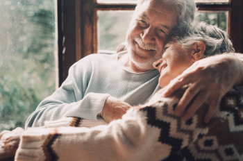 Elderly couple sitting closely, leaning into each other in an embrace