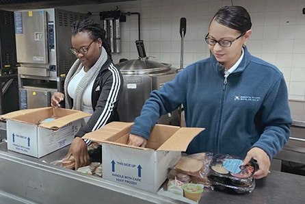 Two female Eisai employees in a parking lot holding a sign saying delivering meals on wheels