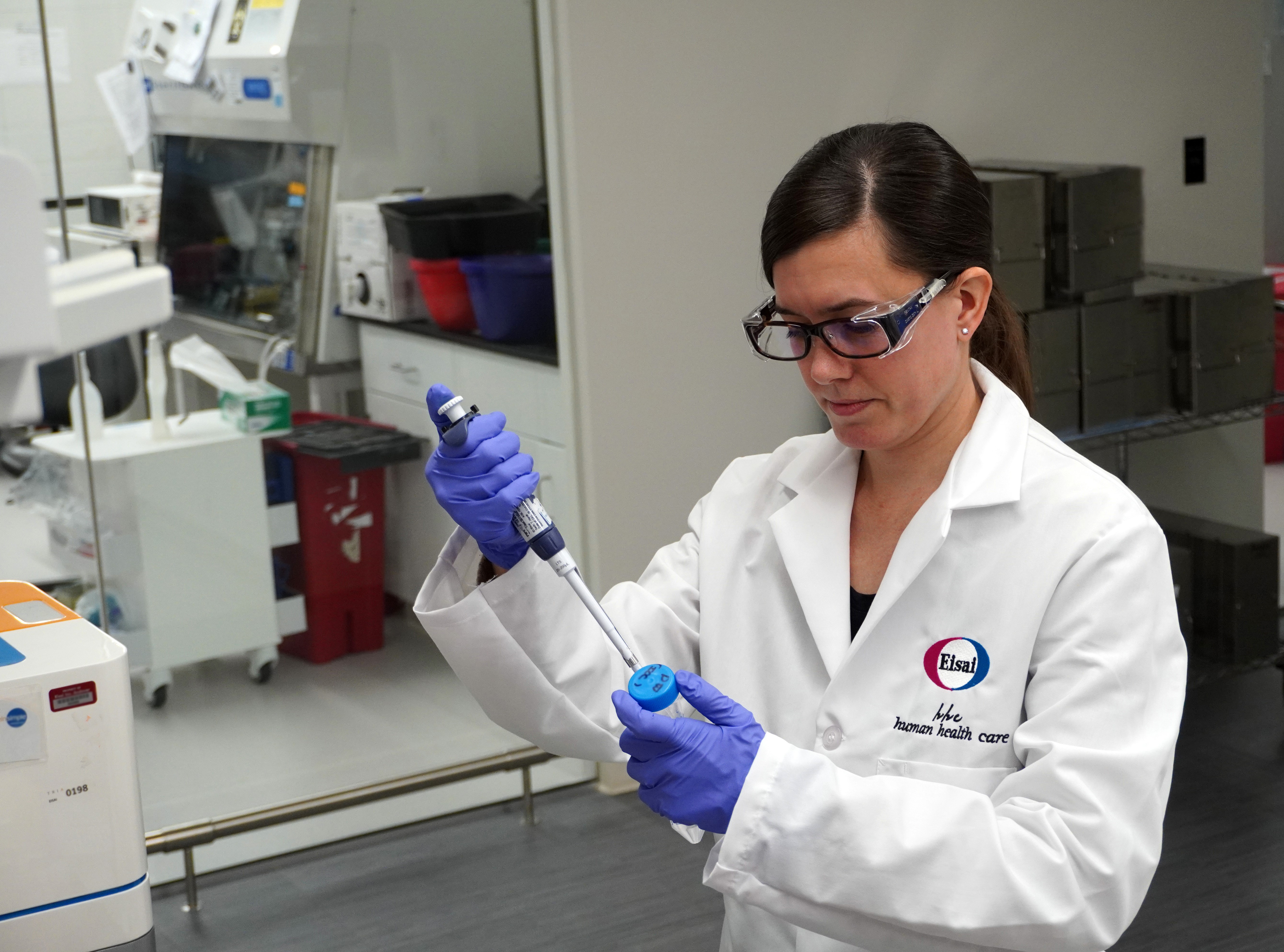 A female scientist wearing an Eisai lab coat, pippetting liquid into a conical tube