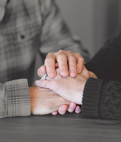 An elderly couple with the woman standing behind the man wrapping her arms around him