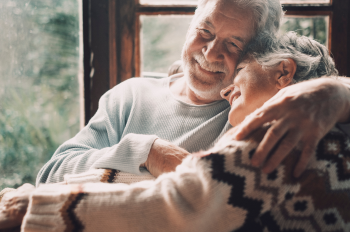 Elderly couple sitting closely, leaning into each other in an embrace Elderly couple sitting closely, leaning into each other in an embrace