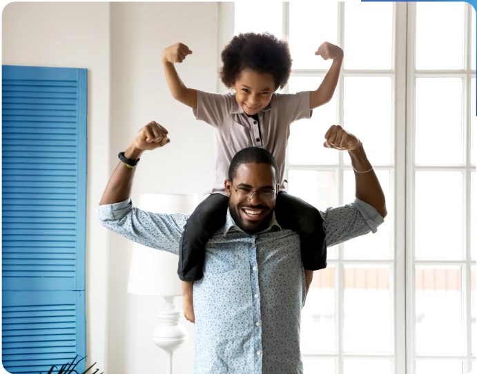 A child sitting on the shoulders of a man in a sunny room. Both are smilling and are flexing their biceps.